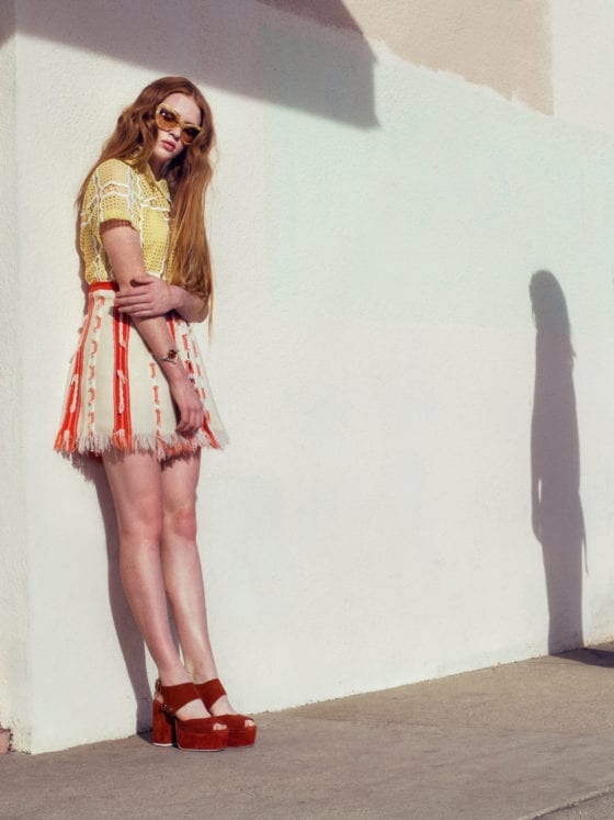 A woman leaning against a white wall with the shadow of another person on the wall