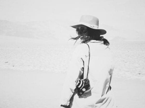 A black and white photo of a woman standing out in the sand dunes