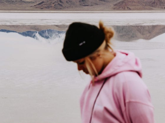 A close up of a blurred woman wearing a hoodie with a mountain in the background