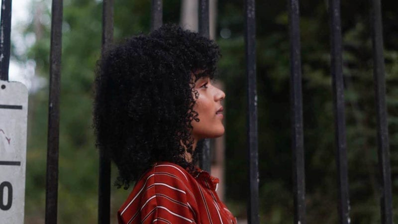 An AfroLatina woman with curly hair standing by a gate