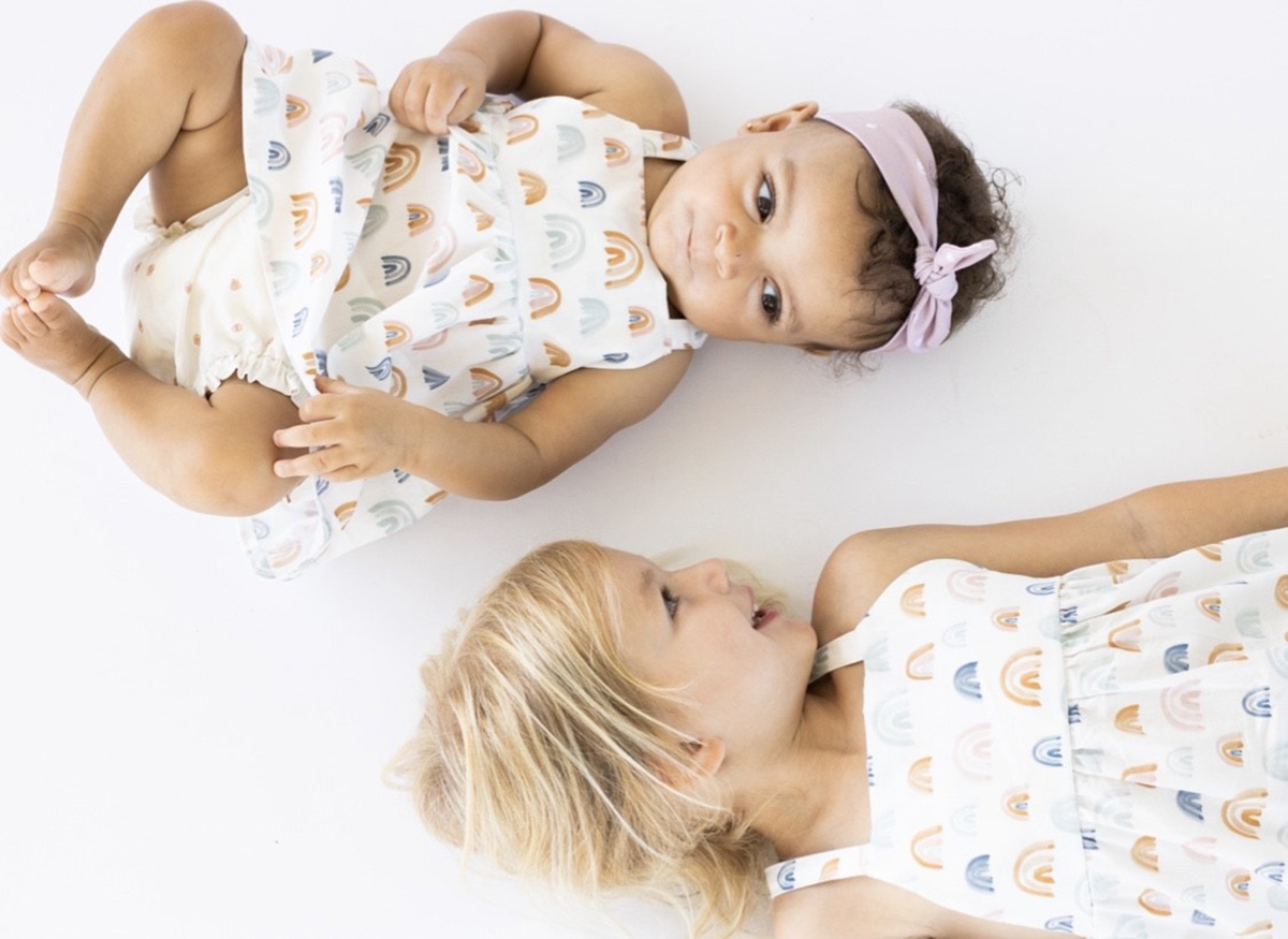 Two little girls lying down looking at each other as their bodies face different directions