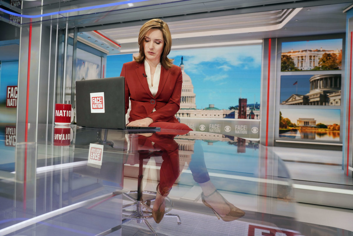 A woman sits at her news anchor desk as she works on her laptop