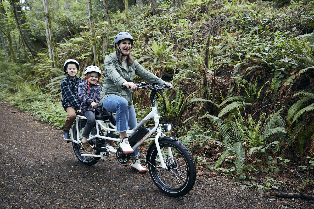 A mom and two boys riding a three-seat bike