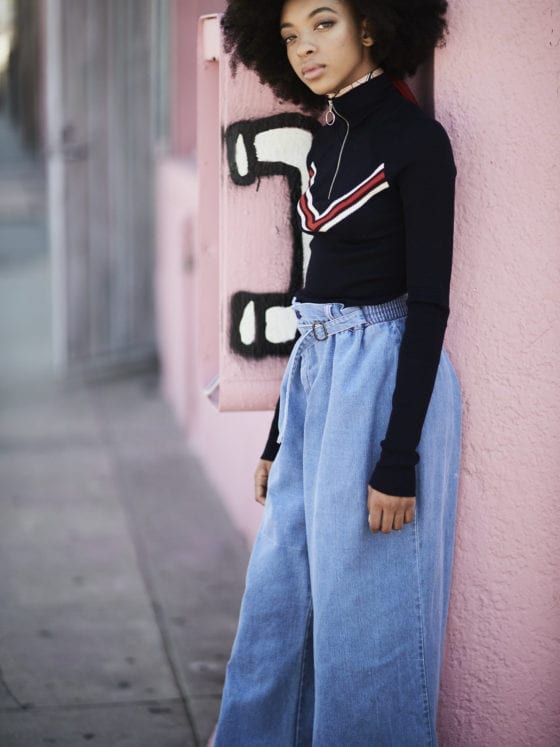 A girl with an afro wearing a sweater and high-waist denim