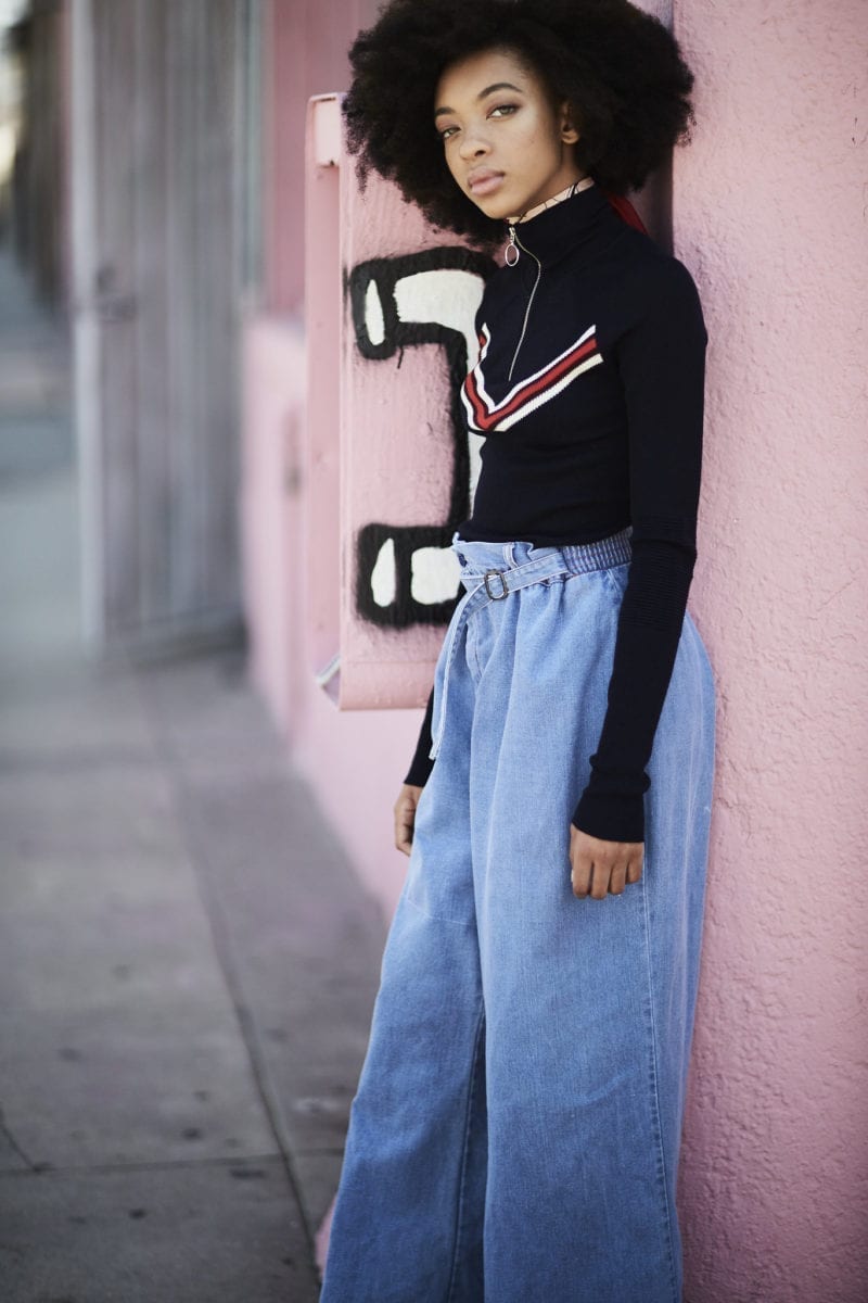 A girl with an afro wearing a sweater and high-waist denim