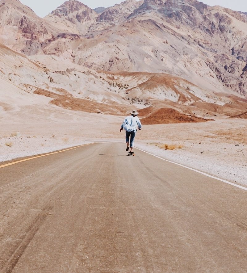A woman skating on an empty road toward the mountains in the background