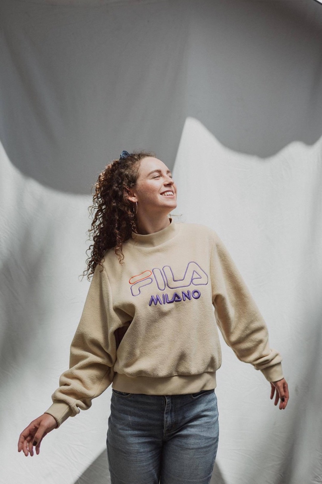 A smiling woman in a Fila sweatshirt looking to her right