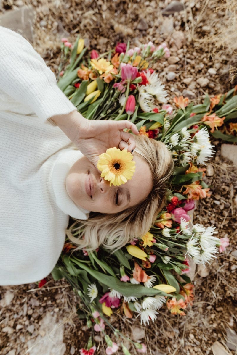 A woman wearing a sweater sitting atop flowers on a