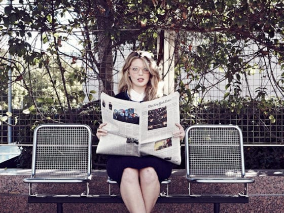 A woman holding a newspaper as she sits on a bench reading