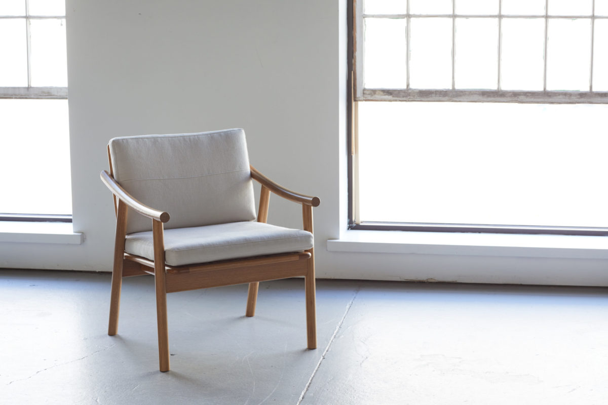 A nude color chair in an empty room with windows that is well lit