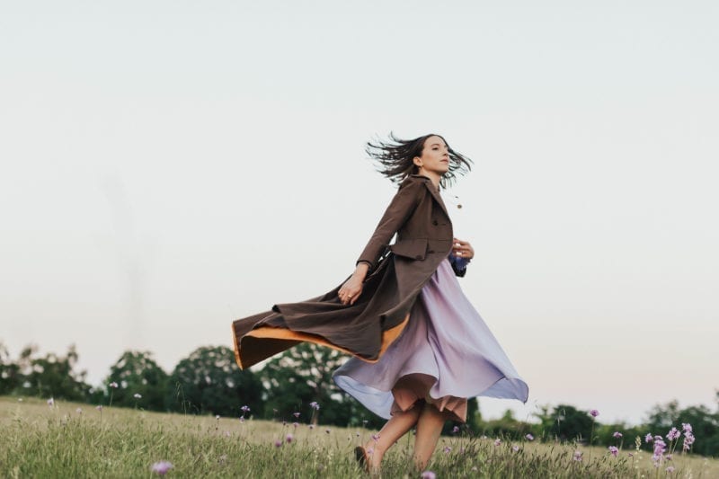A woman in a dress and jacket dancing in a field