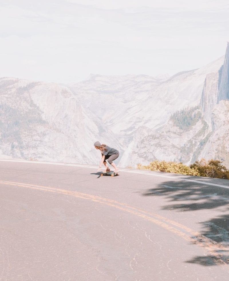 A woman skateboarding down a road near a mountain