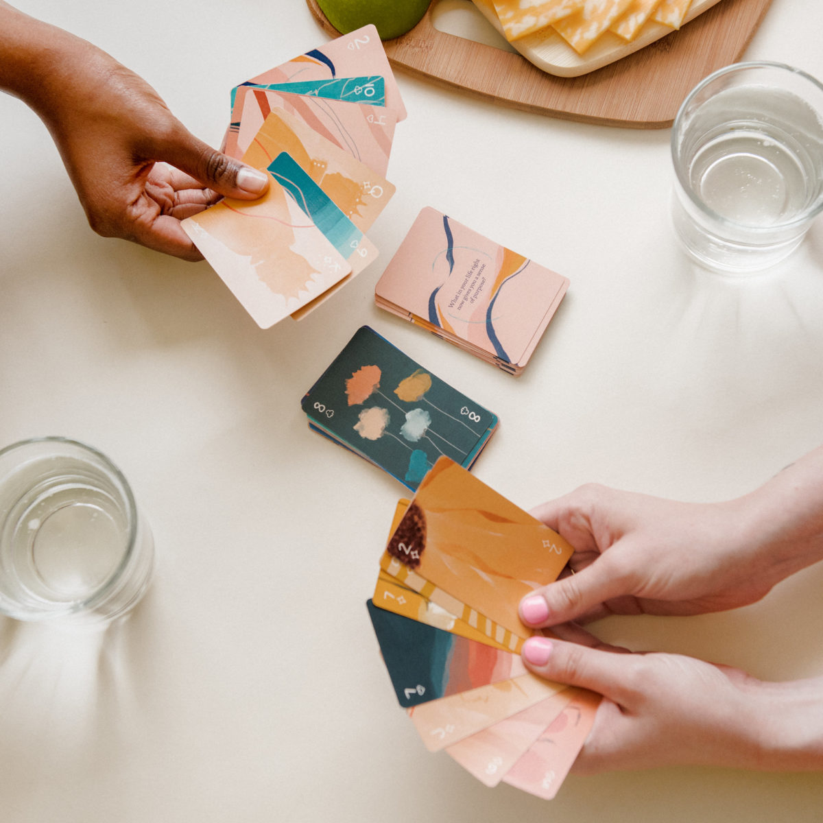 A close up of two hands holding playing cards at a table with food on it