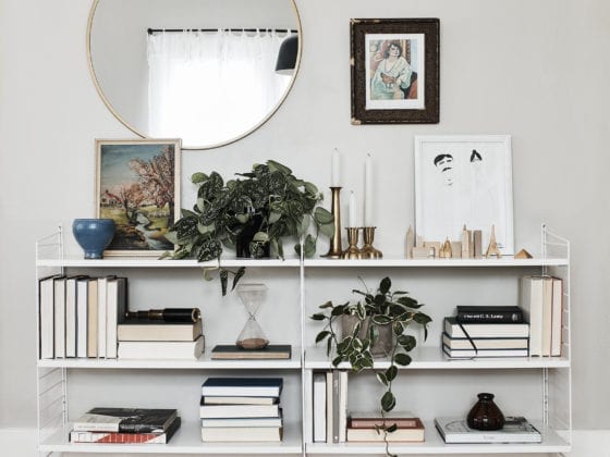 A book stand with greenery on it and a mirror hanging on the wall behind it