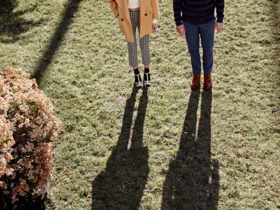 A man and woman standing in the sun on a lawn with their shadows in front of them