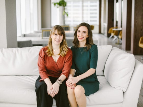 Two women in professional attire seated on a couch