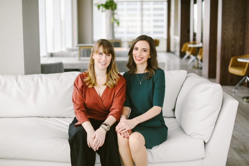 Two women in professional attire seated on a couch