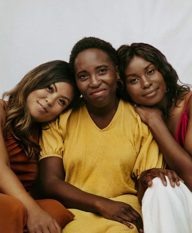 Three smiling women leaning on each other's shoulders