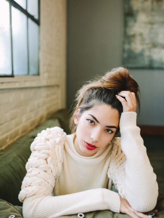 A woman in a cozy sweater leaning on the arm of a couch