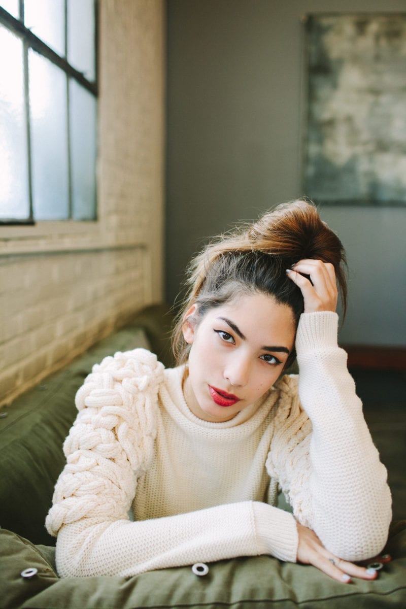 A woman in a cozy sweater leaning on the arm of a couch