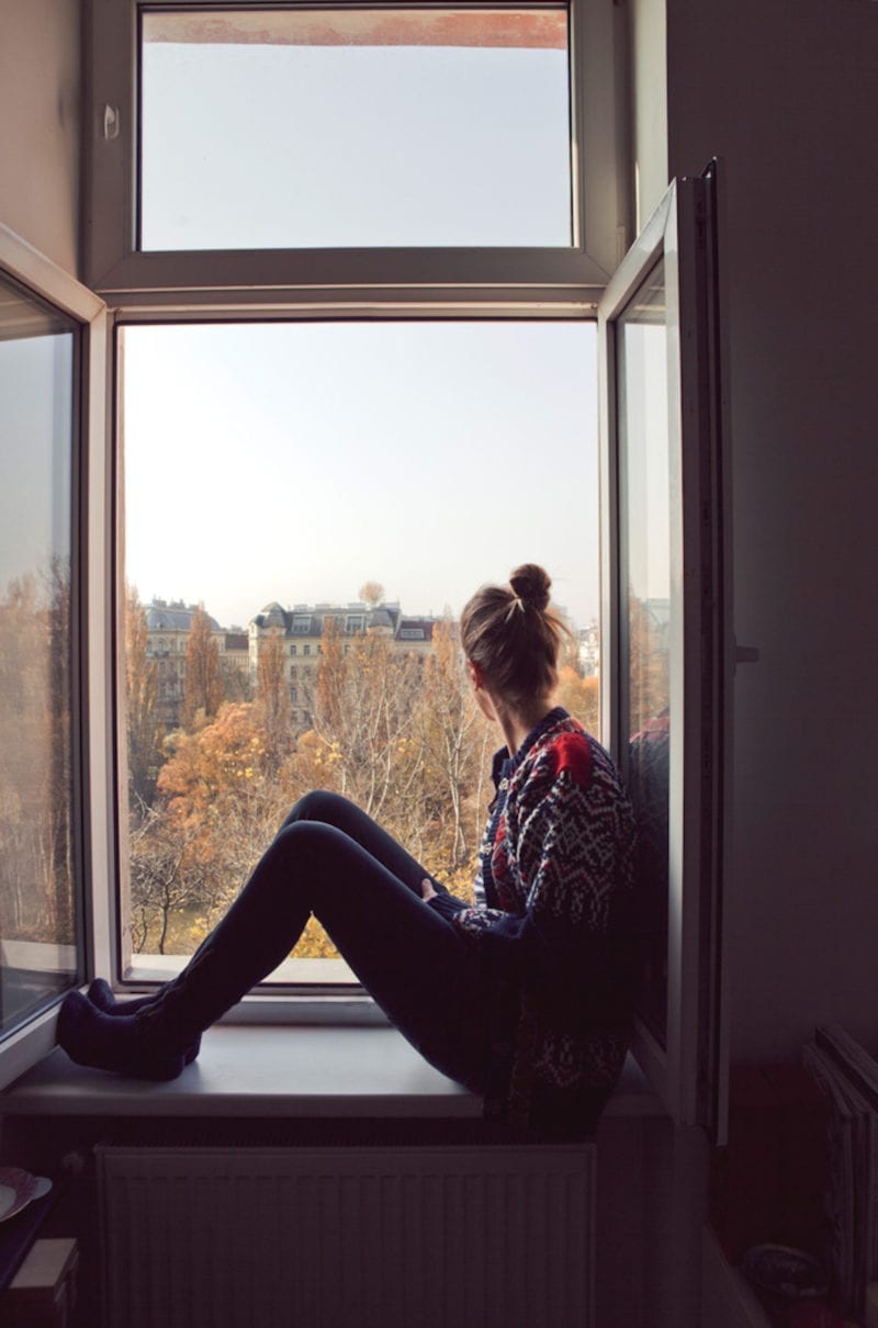 A woman seated in a window sill looking out at the skyline