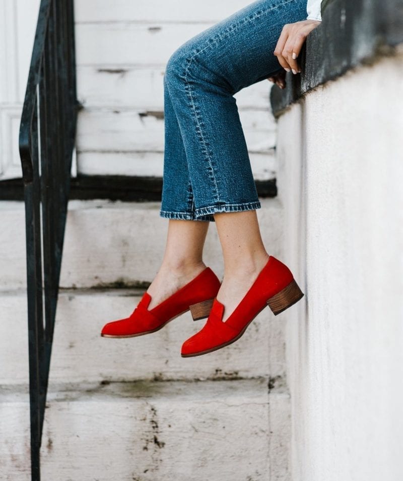 A woman with red shoes as her feet dangle over a banister