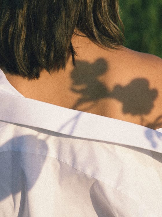 A woman with an off-the-sholder shirt with the reflection of a flower on her shoulder