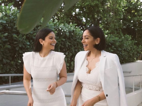 Two laughing women standing outside and wearing all white outfits