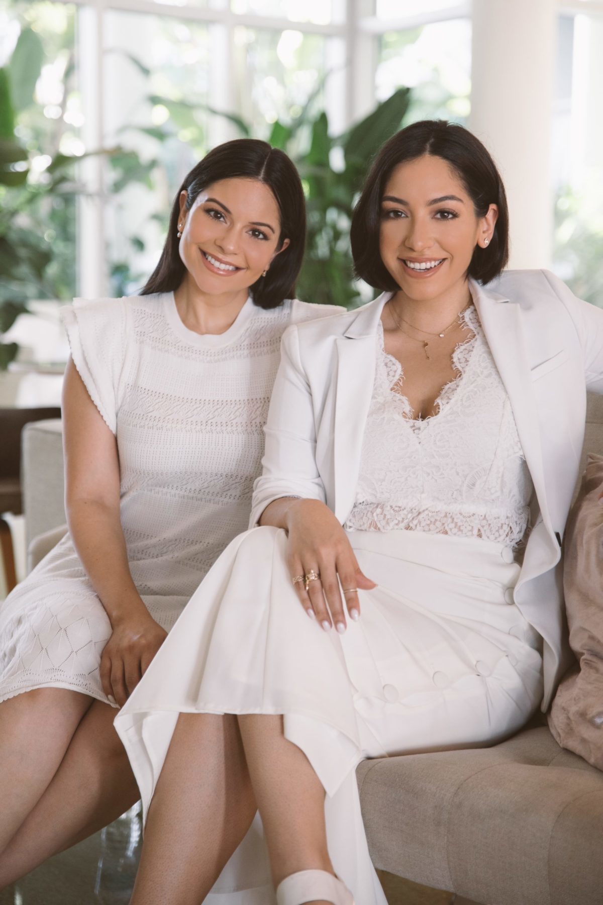 Two women dressed in white smiling as they sit on a sofa
