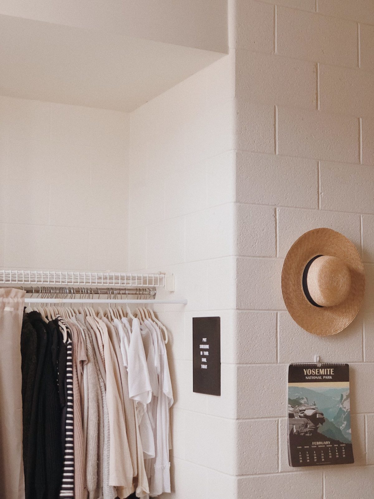 A rack of clothes and a hat hanging on a wall with a Yosemite poster underneath
