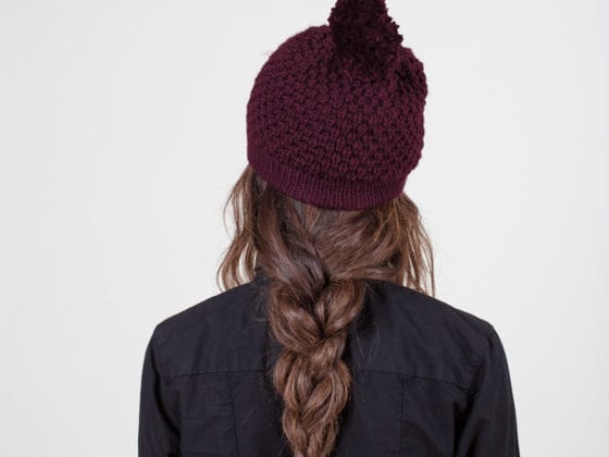 The back of a woman wearing a beanie with her hair in a braid