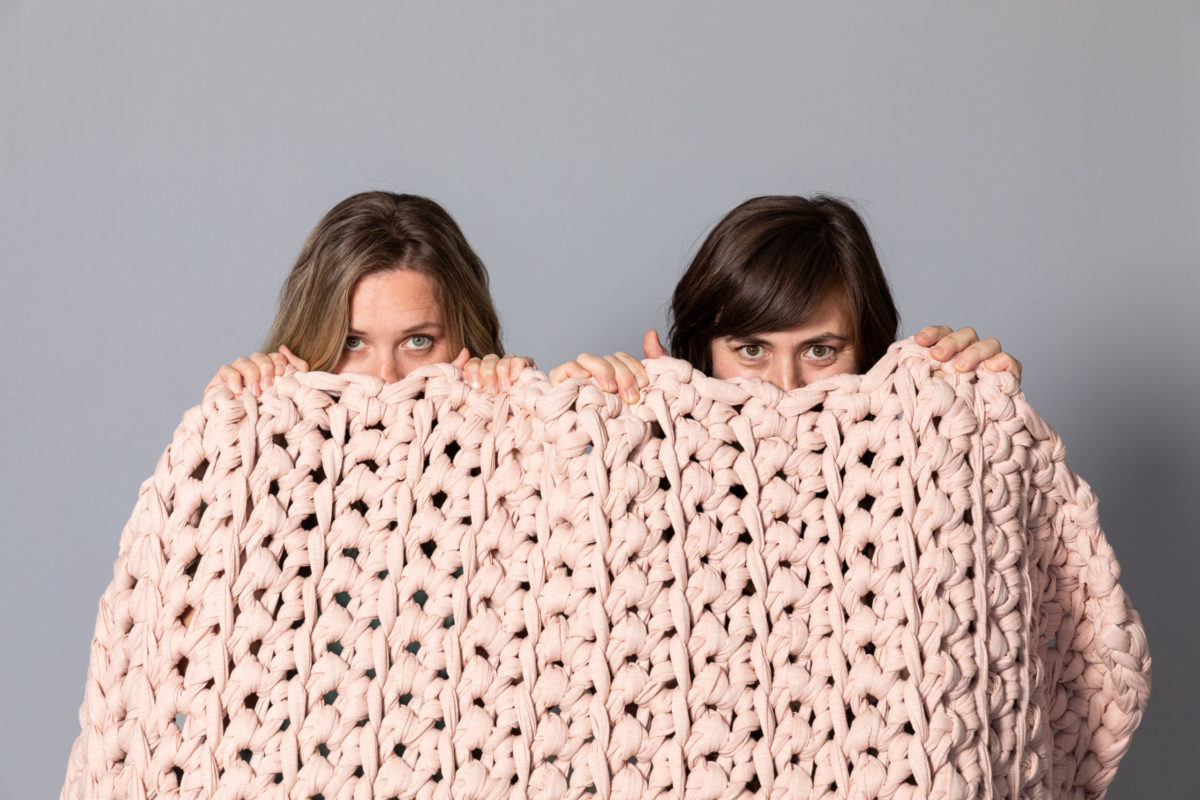 Two women peering over a blanket