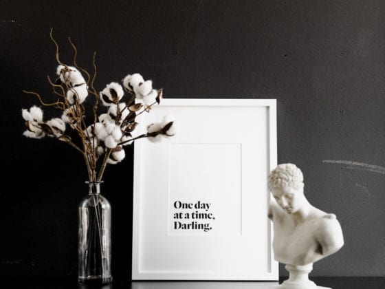 A print that says "One day at a time, Darling" next to a vase of flowers and a sculpture