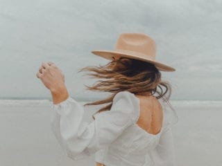 A woman wearing a fedora and turning as her hair flips in the wind