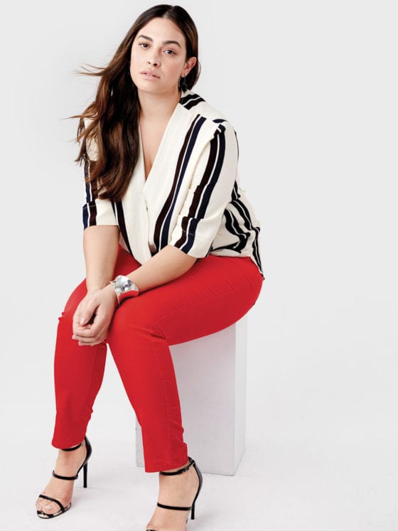 A woman in red pants and a striped shirt sitting on a cylinder shaped box
