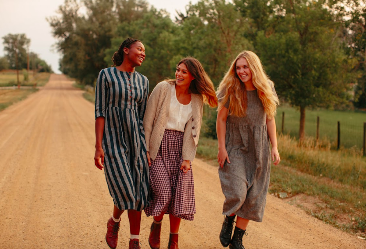 Three smiling women walking along a dirt road