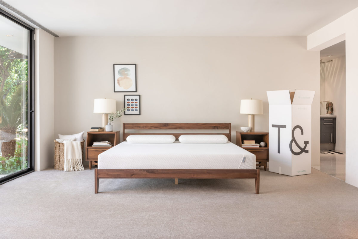 A wooden bed frame and queen sized mattress in a bedroom with nude colored walls