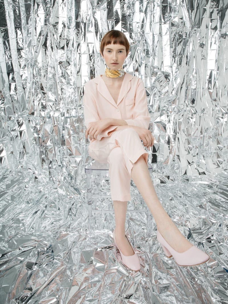A woman in a pink suit sitting in a room with aluminum foil background