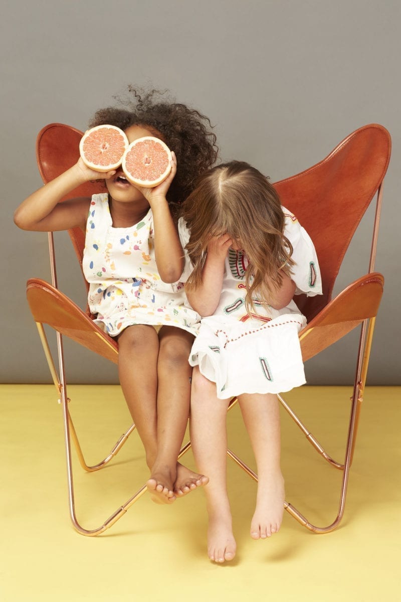 Two little girl sitting in an orange chair covering their faces, one covering hers with grapefruit