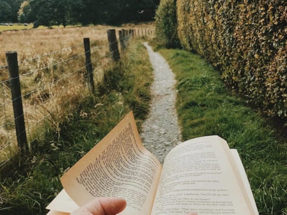 A woman's hand holding out a book along a gravel trail