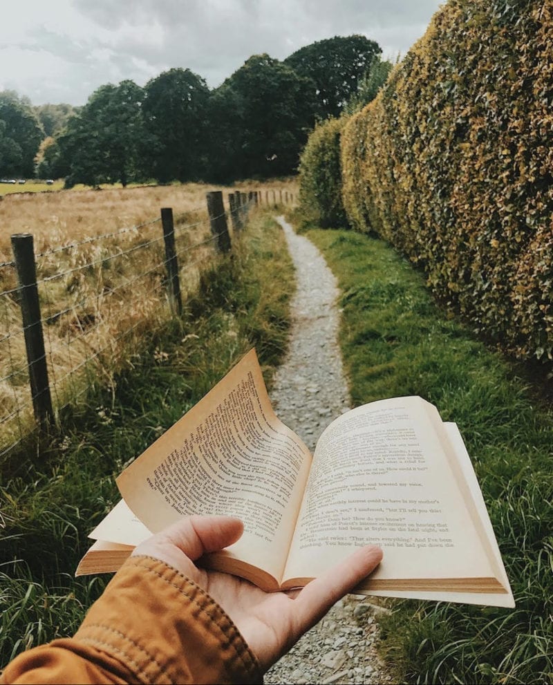 A woman's hand holding out a book along a gravel trail