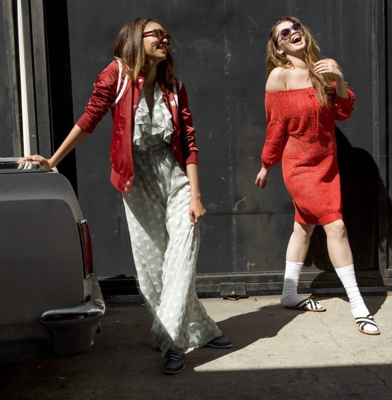 Two women laughing as one leans against the bumper of a car