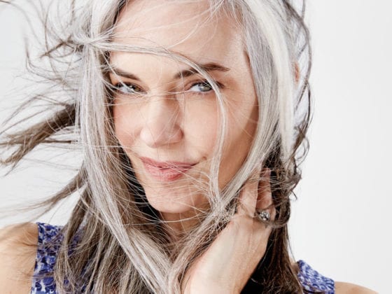 A smiling woman whose gray hair is blowing around her face