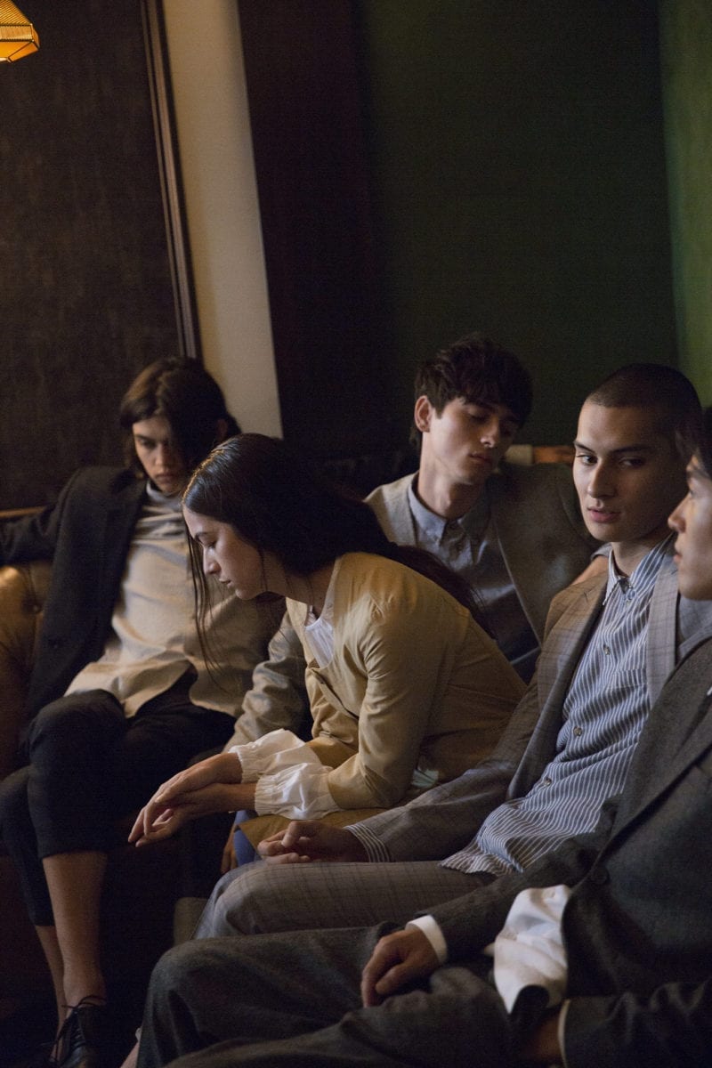 A group of five young adults seated on a couch in professional attire