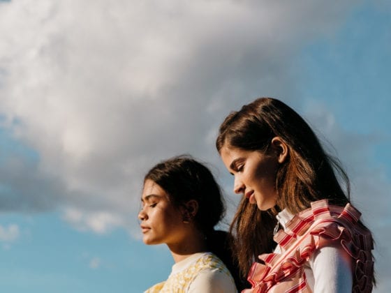 Two women standing side by side outside under the clouds