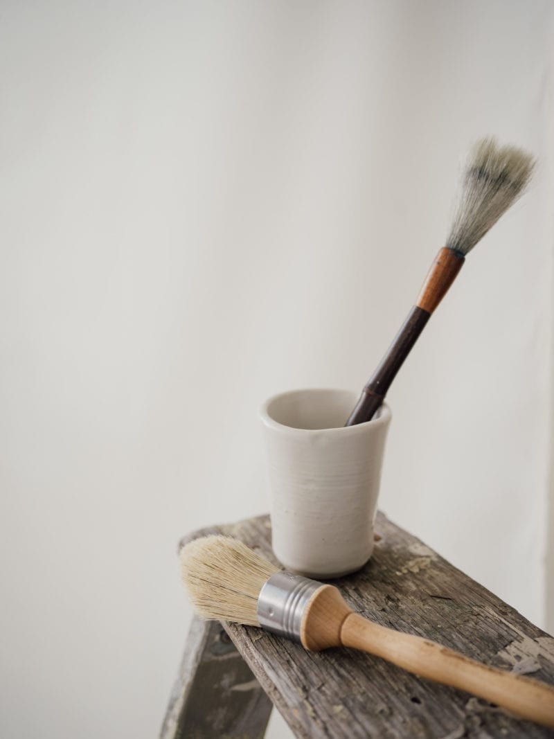 A cup with a paint brush in it and another paint brush beside it