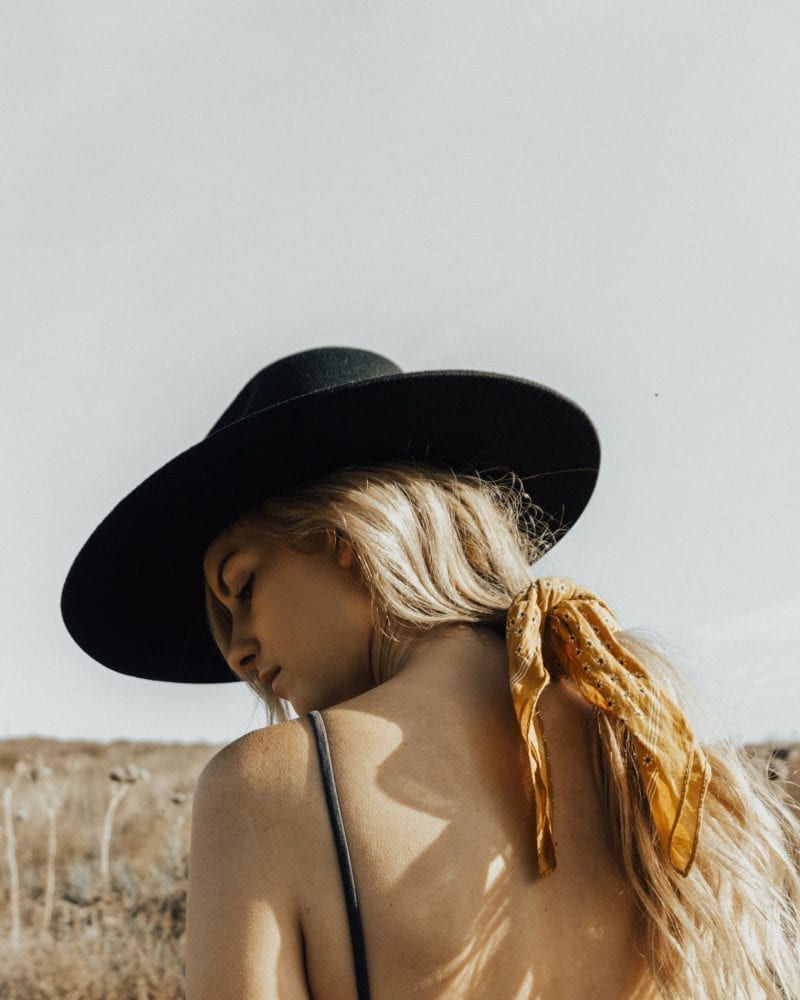 An outdoors photo of a woman in a fedora looking over her shoulder