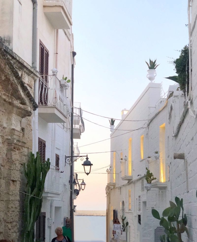 a view of a narrow alleyway between two white buildings that leads to the ocean
